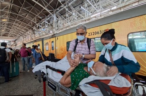 Arogyasewa staff assisting an elderly patient on a medical stretcher for a high-speed train ambulance transfer via Vande Bharat Express.